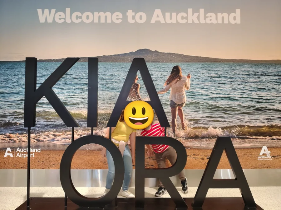 Two kids (with their faces covered by an emoji) posing next to a Kia Ora sign in Auckland Airport